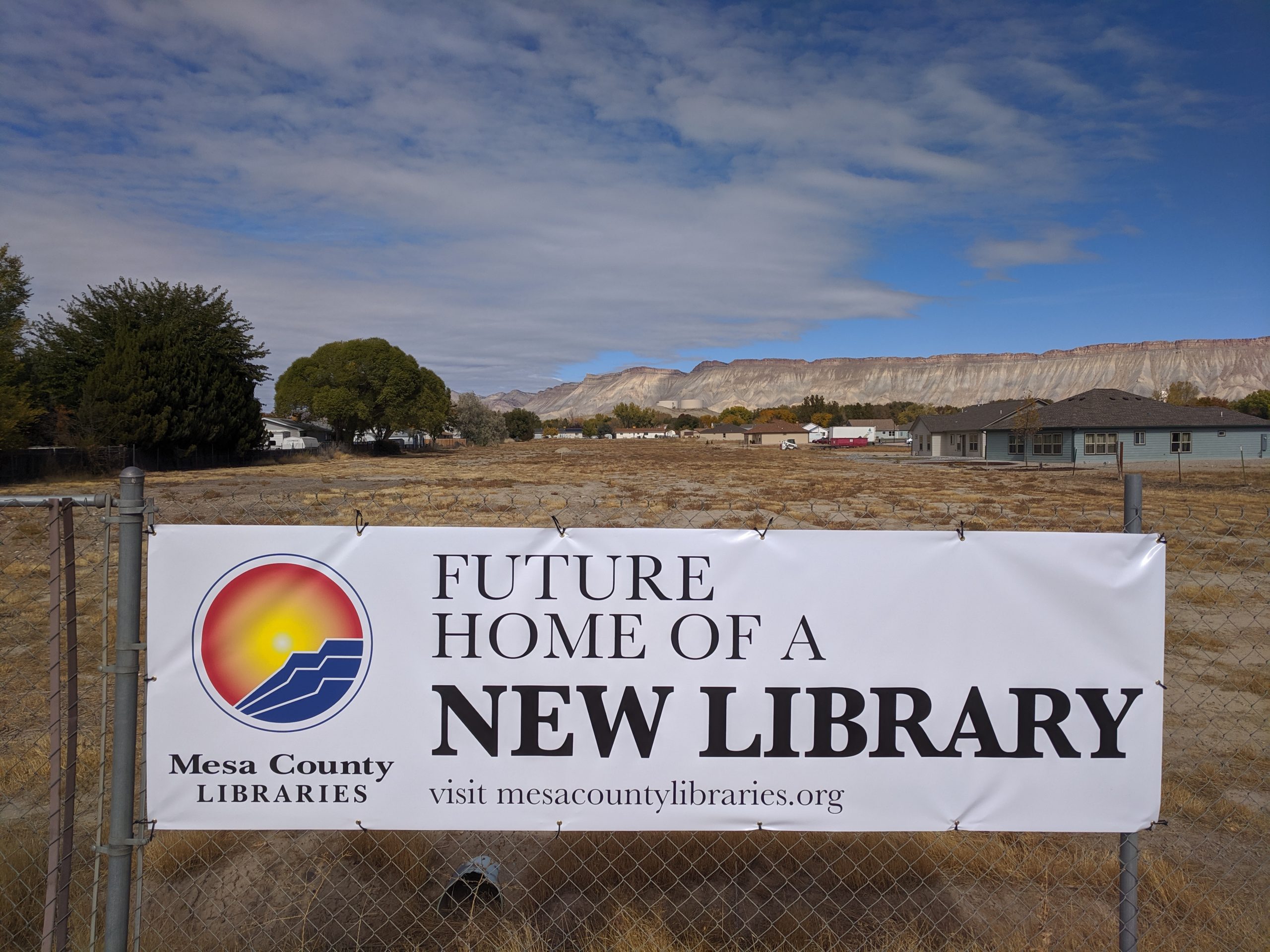 Open field with "Future Home of a New Library" sign in foreground