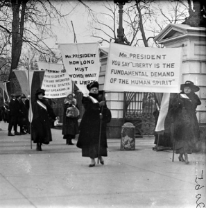 Old photo of women marching the streets with picket signs in favor of suffrage.