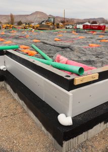 Segments of pipe and materials such as rebar, tarps, and sandbags lie atop an area bordered by forms for concrete.