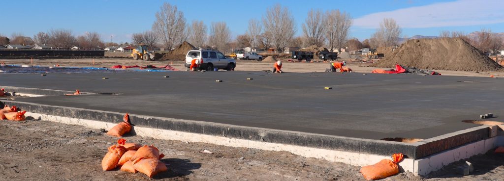 Several construction workers use hand-held tools to smooth a flat slab of concrete.