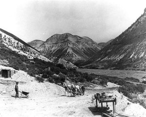 Photo depicting an early shale mining operation in Parachute Creek. Workers can be seen hauling shale by wheelbarrow and by horse-drawn wagon.