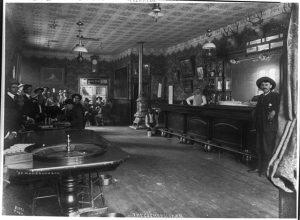PHOTO ID: The Cosmopolitan Saloon and Gambling Hall in Telluride. A roulette wheel sits near the foreground on the left of the image with several men playing cards behind. The right side of the image includes the barkeeper and town sheriff.
