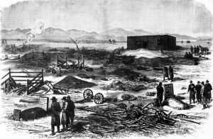Image I.D. - Illustration depicting the ruins of the White River Indian Agency after the Meeker Incident. Several men surround a grave marked "N. C. Meeker" near the foreground, with trashed equipment and smoldering buildings in the background.