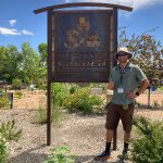 photograph of gardener in residence, Zachary Freeburg, standing in a garden and next to a sign that says Discovery Garden.