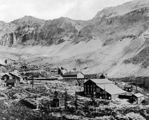 Black and white photograph of the Tomboy Mine and Mill in the Savage Basin near Telluride. The basin is notable for its dramatic and uneven geography with several structures built in some of the flatter sections. 