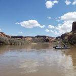 A lone kayak floating on the Colorado River surrounding by red rock canyons.