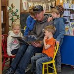 man reading a book to four children